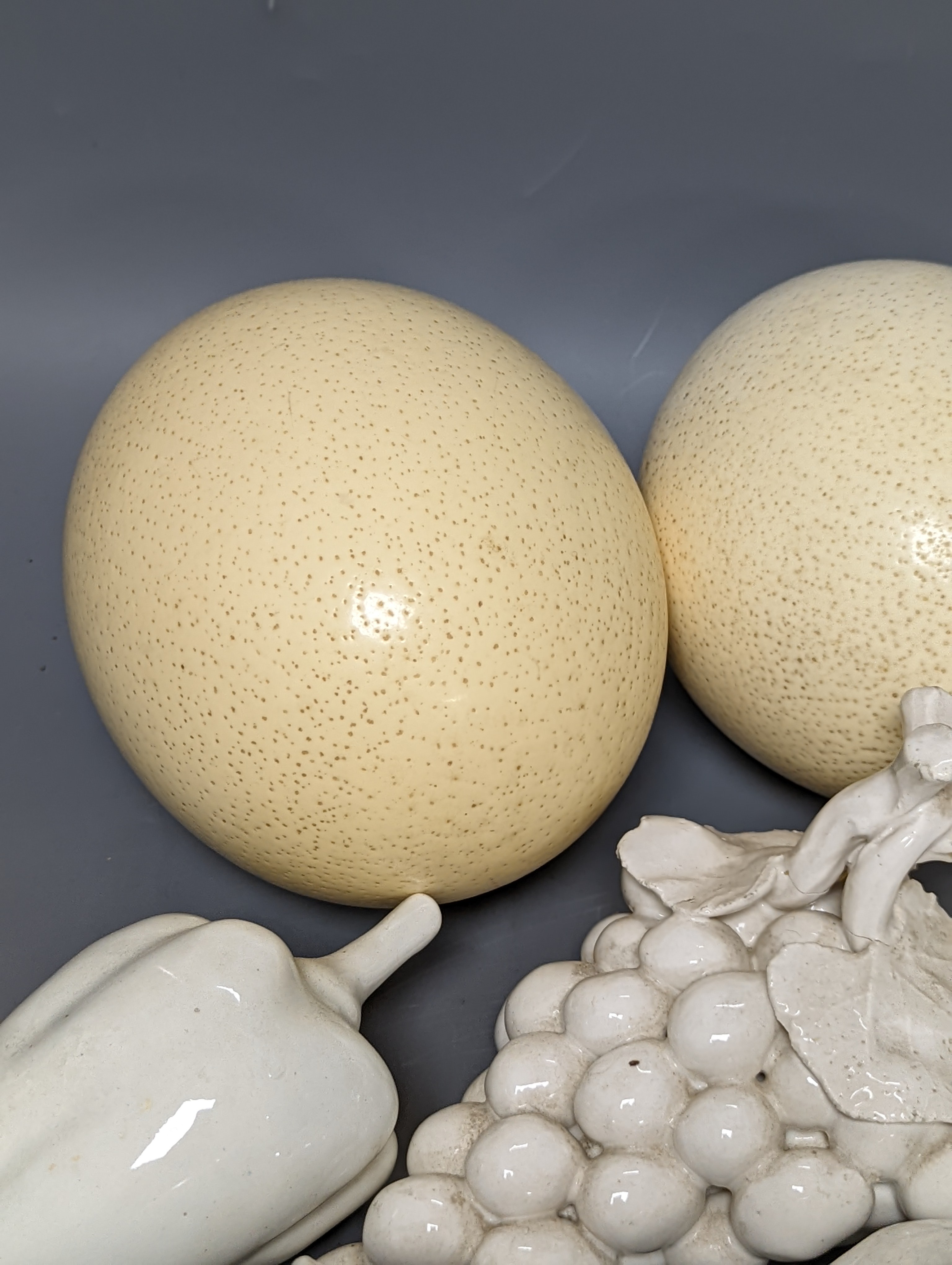 A decorative collection of tin glazed model fruits, together with three ostrich eggs